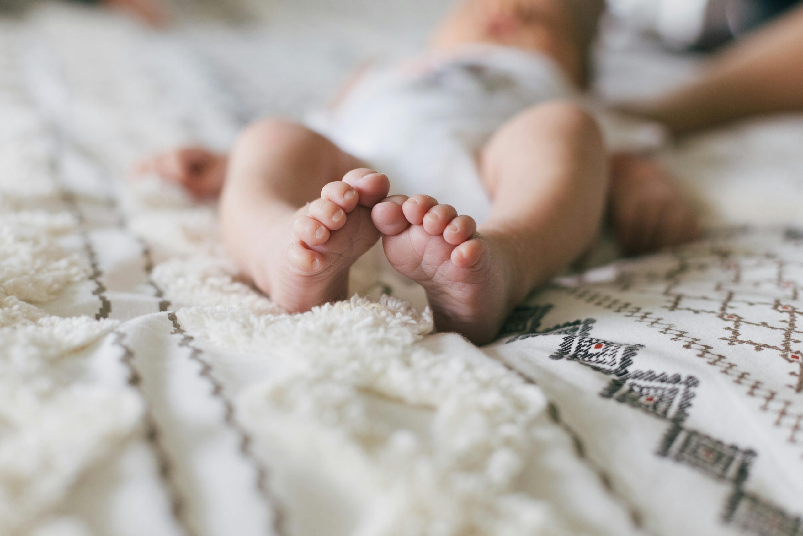 Soft close-up of a newborn's feet resting on a patterned blanket, capturing innocence.